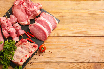 Slate plate with slices of raw pork meat, spices and tomato on wooden background