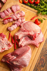 Board with slices of raw pork meat and vegetables on wooden background