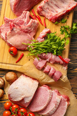 Board with slices of raw pork meat and vegetables on wooden background