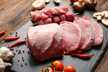 Slate plate with raw pork meat, spices and vegetables on wooden background, closeup