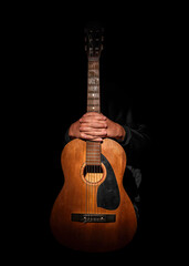 A staged photograph of a boy with a guitar on a black background.
