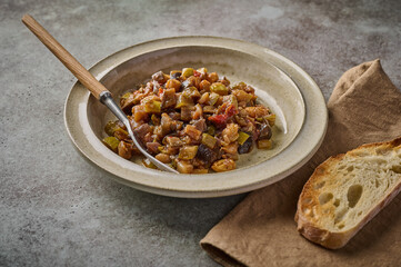 Homemade traditional Sicilian caponata with eggplant, zucchini, tomatoes, olives and ciabatta bread. Close up, copy space