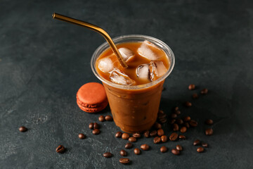 Plastic cup of iced coffee with macaroon on dark background