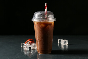 Plastic cup with coffee and ice on dark background