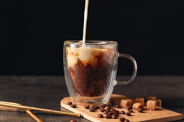 Pouring milk into cup with cold coffee on dark background