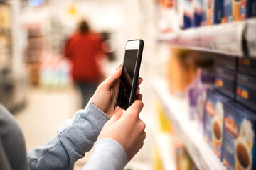 Woman's hand holding smart phone on supermarket blur background.