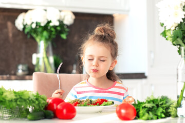 child girl enjoy eating healthy salad with closed eyes from a large plate at home in white sunny...