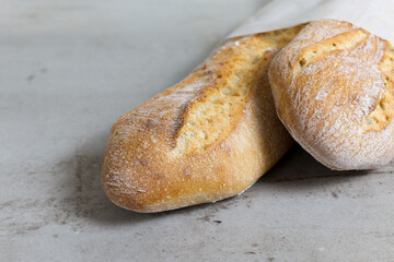 close up crusty baguettes, baked bread on grey stone table background. French bread. eco-friendly paper packaging. 