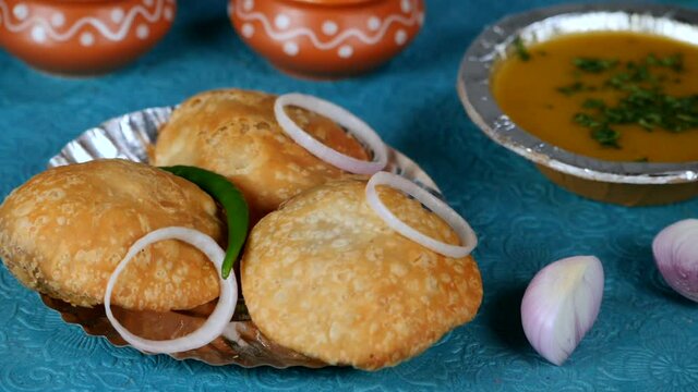 Spicy green chili falling on a plate with Khasta Pyaaz Kachodi and onion rings - Street Food India. Closeup shot of Aloo Ki Sabzi  raw onion slices  and earthen bowls kept together on a floral mat