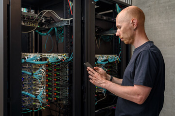 Man data center technician performing server maintenance. Using mobile phone to troubleshooting