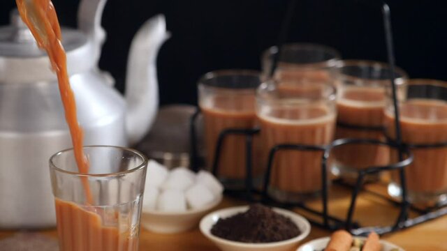 Boiling hot flavored tea pouring in transparent glass - refreshing hot  drink  Indian Chai. Closeup shot of sugar cubes  tea leaves  glass holder  and Indian spices kept together - tea-making ingre...