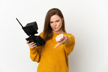 Teenager girl holding a drone remote control over isolated white background showing thumb down with negative expression