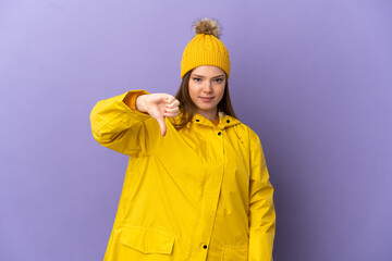 Teenager girl wearing a rainproof coat over isolated purple background showing thumb down with negative expression