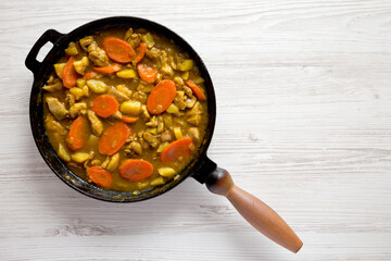Homemade Japanese Chicken Curry in a cast-iron pan on a white wooden background, top view. Flat lay, overhead, from above. Copy space.