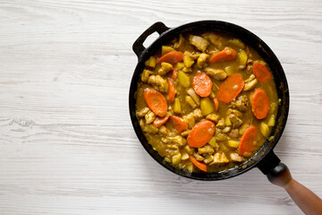 Homemade Japanese Chicken Curry in a cast-iron pan on a white wooden surface, top view. Flat lay, overhead, from above. Space for text.