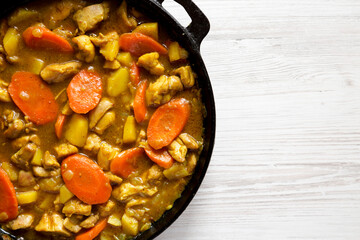 Homemade Japanese Chicken Curry in a cast-iron pan on a white wooden background, top view. Flat lay, overhead, from above. Copy space.