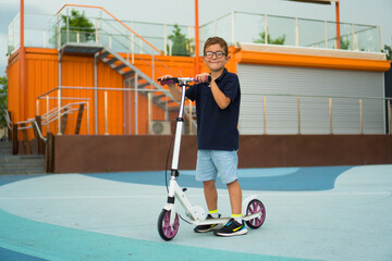 A boy is standing next to kick scooters on the sports court in the city park.