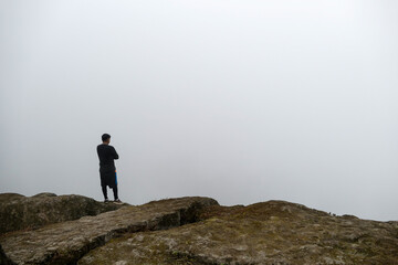 Naklejka na ściany i meble Man standing on cliff in a valley, looking at the mist.