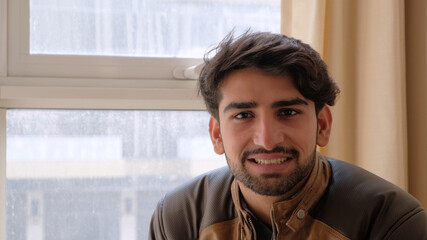 Handsome smiling Indian man looking at the camera against a wall with plants in pots