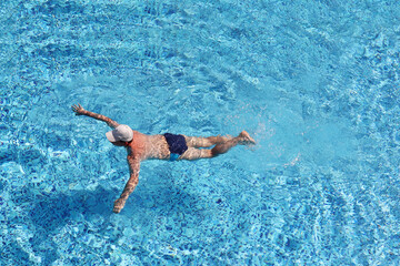 Man in baseball cap swimming in the pool water, top view. Water sports, beach vacation