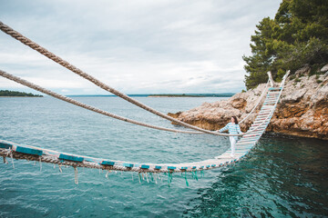 woman crossing suspension bridge sea on background