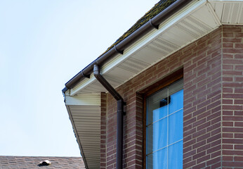 Corner of house with old roof from bituminous tile with moss and rain gutter. Metallic Guttering System, Guttering and Drainage Pipe Exterior