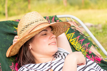 Smiling girl in straw hat and striped t-shirt lies on a cot outdoors