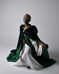 Full length portrait of pretty African woman wearing long green medieval fantasy gown, kneeling...