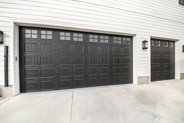 Two black garage doors with window panels and wall lighting - obrazy, fototapety, plakaty