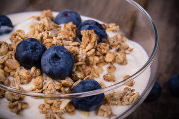 Yogurt with granola and blueberries in a glass bowl. Healthy breakfast over old wood background. 