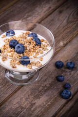Yogurt with granola and blueberries in a glass bowl. Healthy breakfast over old wood background. 