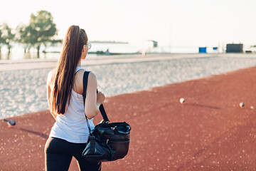 Young woman with sports bag walks on sports ground