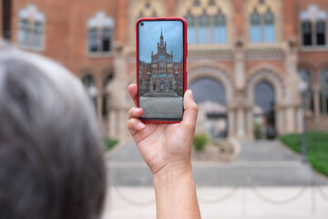 Naklejka premium Woman take photograph with smart phone to hystoric building in Barcelona. Traveler, tourism, discover, caucasian female