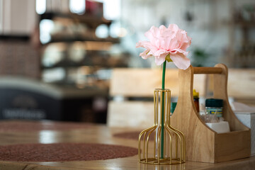 Naklejka na ściany i meble An artificial pink rose flower branch in luxury designed vase in place on dining table. Interior decoration object photo. Close-up and selective focus. 