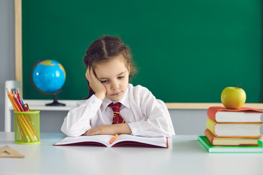 Sad Schoolgirl Looks At A Book While Sitting In Class. A Math Problem In A Child At School.