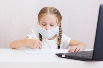 A LITTLE GIRL IN A MASK SITS AT A TABLE AND DRAWS, WRITES. STUDENT. SCHOOL. THE FIRST OF SEPTEMBER. HOME QUARANTINE