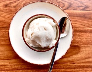 Craft ice cream made with coconut and almond on a white plate, with a teaspoon next to it. Top view.

I