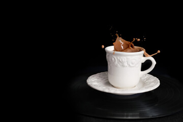 closeup of cappuccino coffee in a white cup and saucer on a black background with splashes and drops of liquid in all directions, the concept of a cafe menu, coffee time