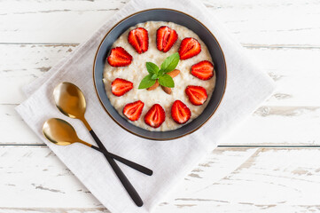 Oatmeal Porridge with Strawberries in dark bowl. Healthy Breakfast with Oatmeal and Fresh Organic Berries, top view, copy space.