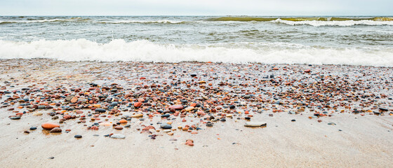 A lot of varieties of sea rocks on a sandy beach against the background of a restless Baltic Sea with waves