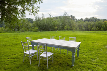 White table with chairs under tree on lawn. White table with chairs located on green grass under lush tree on summer day in field