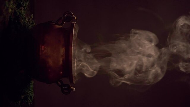 The witch's smoking cauldron on dark background. Vertical video.