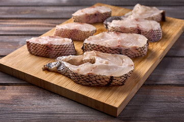 Pieces of sliced white raw fish macrourus on a wooden cutting board on wooden rustic background. Close up