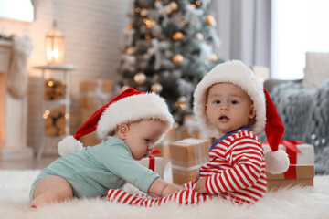 Fototapeta na wymiar Cute children in Santa hats on floor in room with Christmas tree