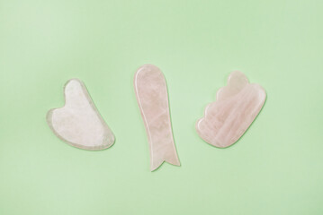 Gua Sha Massagers on Green Background Pink jade stone for face and body Horizontal Flat lay Top view Copy Space