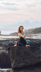 Naklejka na ściany i meble Girl doing yoga by the sea while sitting on a stone.