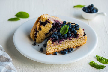 Sliced blueberry sponge cake on a white plate on a light concrete background. Baking berries.