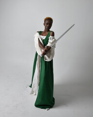 Full length portrait of pretty African woman wearing long green medieval fantasy gown holding ...