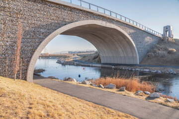 Two trail paths on both sides of the lake under an arched bridge with gabion walls