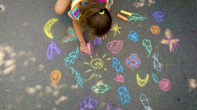 The child draws with chalk on the asphalt. Selective focus.